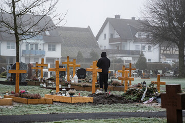 mourning man standing alone on a graveyard full of crosses. 