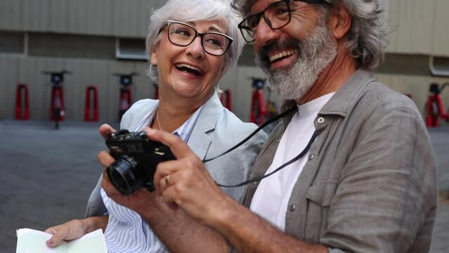 Senior couple holding a map and with a camera - retired travelers are laughing - focus in woman -