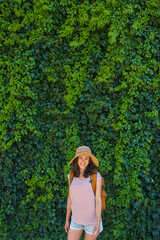 A girl in a straw hat stands near a wall overgrown with ivy