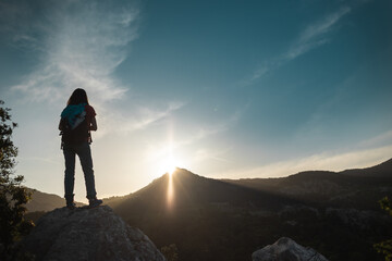 Fototapeta premium The silhouette of a woman with a backpack against the backdrop of a mountain at sunset