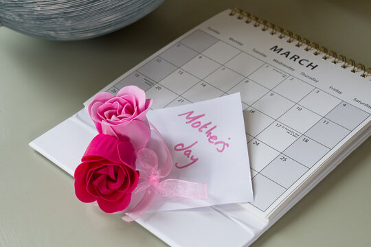 Mothers day reminder calendar with pink roses. March calendar placed on a table with focus on the flowers. Image taken from side on perspective. pretty post it note. Mothering Sunday, March 19th 2023.