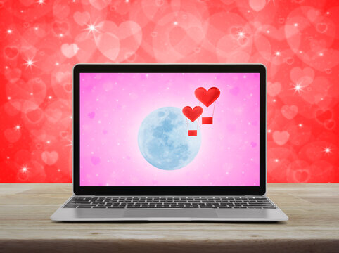 Red fabric heart love air balloon fly over moon and blur pink star background on modern laptop computer screen on wooden table over red wall, Business internet dating online, Valentines day concept