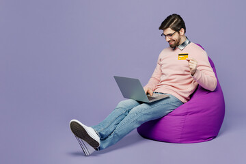 Full body young IT man wear casual clothes pink sweater glasses sit in bag chair use mobile cell...