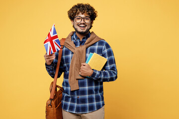 Obraz premium Young cheerful fun teen Indian boy IT student wear casual clothes shirt glasses bag hold in hands books British flag isolated on plain yellow color background High school university college concept.