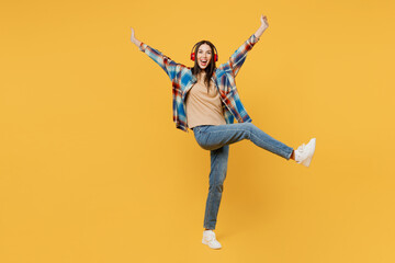 Fototapeta na wymiar Full body young woman wear blue shirt beige t-shirt headphones listen to music dance with outstretched hands raise up leg isolated on plain yellow background studio portrait. People lifestyle concept.