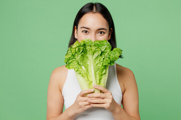 Young woman wear white clothes hold cover mouth with bunch of fresh greens lettuce leaves isolated on plain pastel light green background. Proper nutrition healthy fast food unhealthy choice concept.