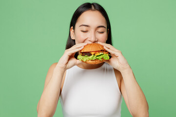 Young happy hungry fun cheerful woman wear white clothes holding eating biting tasty burger...