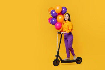 Full body side view happy fun young woman wear casual clothes hat celebrating hold bunch of balloons riding e-roller scooter isolated on plain yellow background. Birthday 8 14 holiday party concept.