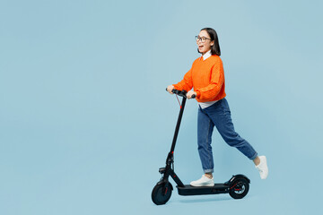 Full body side view cool happy young woman of Asian ethnicity wear orange sweater glasses riding electric scooter isolated on plain pastel light blue cyan background studio People lifestyle concept. © ViDi Studio