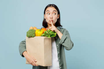 Fototapeta na wymiar Young woman in casual clothes hold brown paper bag with food products say hush shhh be quiet with finger on lip isolated on plain blue cyan background studio Delivery service from shop or restaurant