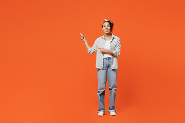 Full body young woman of African American ethnicity she wears grey shirt headband pointing indicate on workspace area copy space mock up isolated on plain orange background. People lifestyle concept.