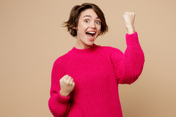 Young happy overjoyed caucasian woman wear pink sweater doing winner gesture celebrate clenching...