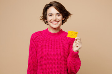 Young happy cheerful fun smiling caucasian woman wear pink sweater hold in hand mock up of credit...