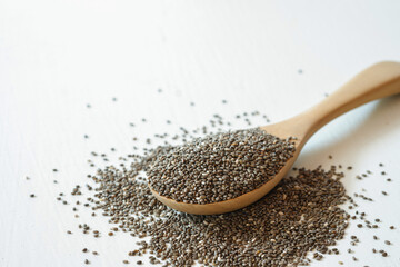 Chia seeds in a wooden spoon on a white background.