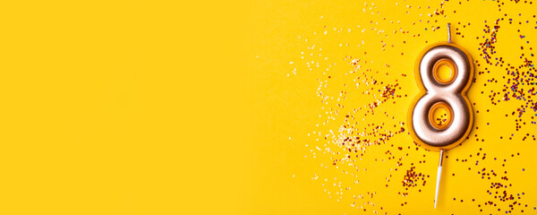 Gold candle in the form of number eight on yellow background with confetti.