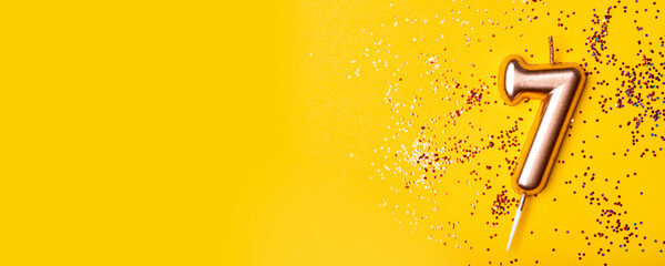 Gold candle in the form of number seven on yellow background with confetti.