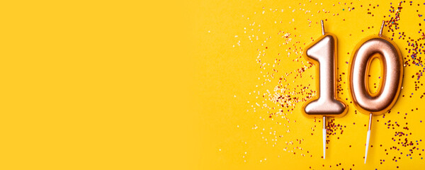 Gold candle in the form of number ten on yellow background with confetti.