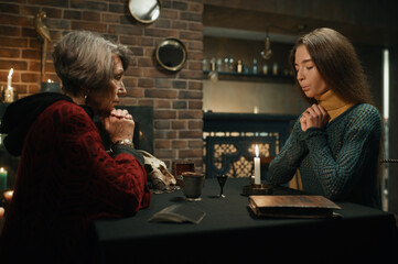 Old gypsy fortune teller and young woman performing magic ritual