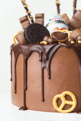 KYIV, UKRAINE - January 15: Birthday cake with brown cream cheese frosting and chocolate drips decorated with Kinder egg toy, Milka and KitKat sweets, Oreo cookies and candies. White background