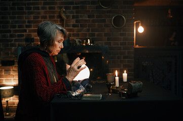 Portrait of old mature fortune teller looking into crystal ball