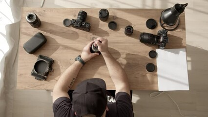 Top down view of desktop where videographer clean dust and dirt from equipment. man in cap work with lens from photo camera or video camera. photographer takes care of equipment. Lens repair service.