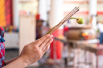 Action of human hand is holding incense stick and lotus flower during pay homage at the temple in...