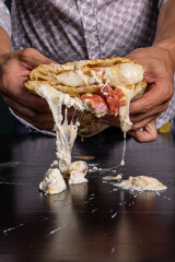 Pizza ripiena napoletana cotta al forno ripiena di ricotta, salame piccante e mozzarella tagliata a metà tenuta in mano da un cliente di una pizzeria 