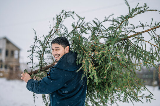 Happy man carrying fir tree in snow