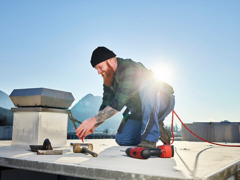 Roofer working with pliers at roof on sunny day
