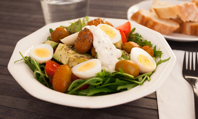 fresh salad of arugula, avocado, cherry tomatoes with olives and quail eggs in white bowl