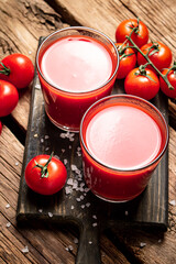 Glasses with tomato juice on a wooden cutting board. 