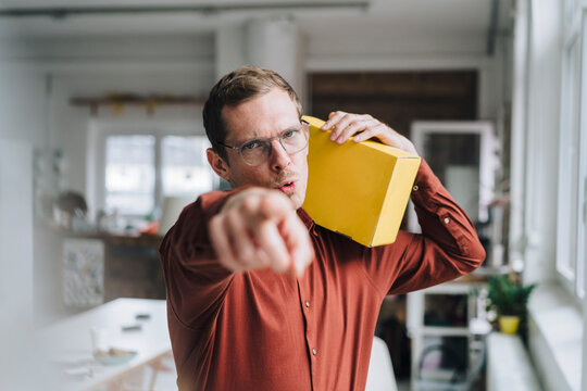 Businessman pointing and holding yellow box in office