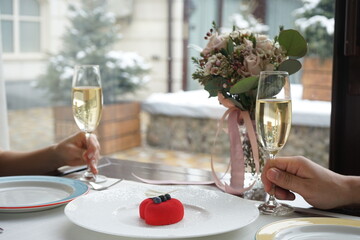 red dessert in the background of a heart decorated with berries in a white plate on the table with a glass of prosecco in hands
