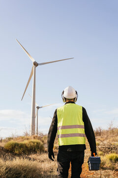 Technician with toolbox standing in front of wind turbines on sunny day