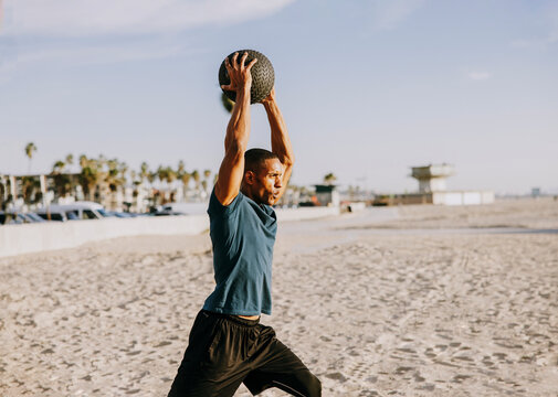 Sportsman with arms raised exercising with ball on beach