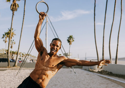 Cheerful sportsman gripping on gymnastic rings at beach