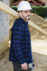 portrait of young carpenter carrying wooden plank over his shoulder