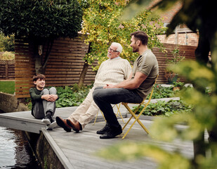 Father, son and grandson sitting at garden pond talking and relaxing