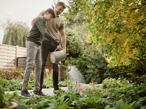 Father and son standing in garden watering plants
