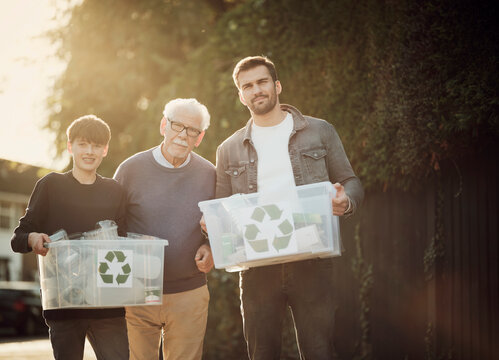 Grandfarher, father and son standing outdoors carrying recycling boxes with separated waste