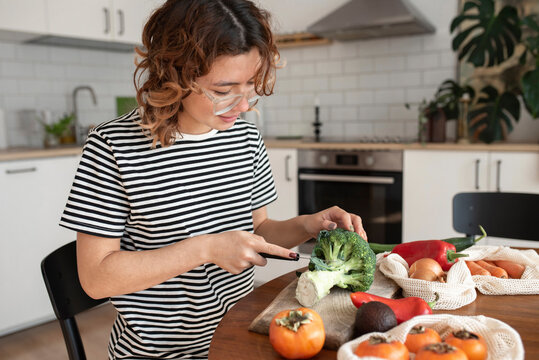 Woman cutting vegetable sitting on table at home