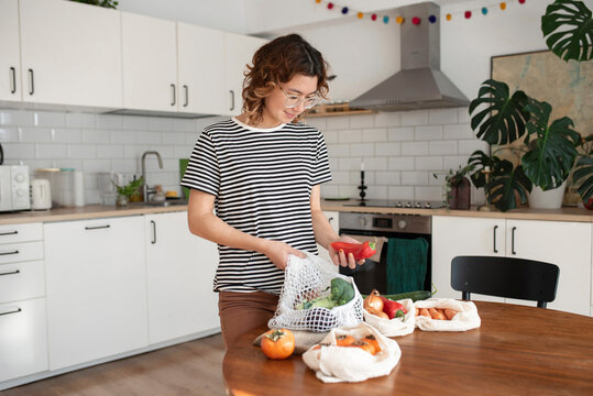 Young woman with vegetables standing by table at home