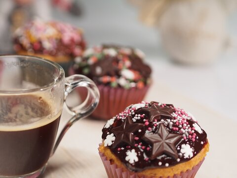 Cupcake with chocolate and chocolate stars, sugar  snowflakes, sugar balls and coffee in transparent cup on wooden white painted table
