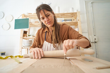 Woman in pottery workshop cutting clay while holding a rolling pin. Handicraft workshop 