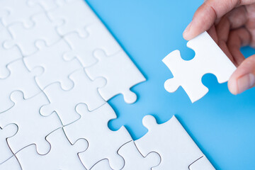 Obraz premium White jigsaw in the hands, The correct solution. Teamwork, Solving and completing the task. Last piece of jigsaw puzzle. Assembling jigsaw puzzle pieces.