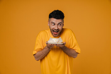 Excited hungry man in holding plate with cake isolated over yellow wall