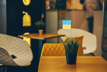 Interior details with Ukraine flag in small potted plant at coffee shop. Life of Ukrainians emigrants or refugees in Europe, support small local business and entrepreneurs.