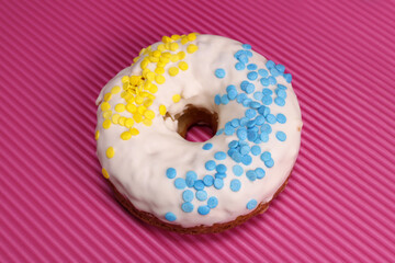 Fresh glazed donut with blue-yellow sprinkling in the colors of the flag of Ukraine on a pink background