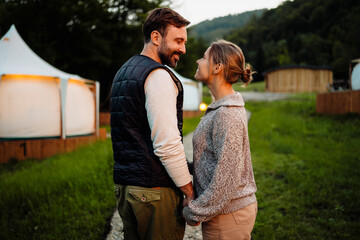 White couple smiling at each other standing near lodging in forest