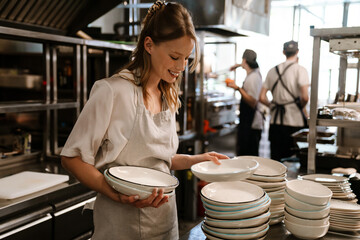 Young blonde woman holding plates while working in restaurant kitchen